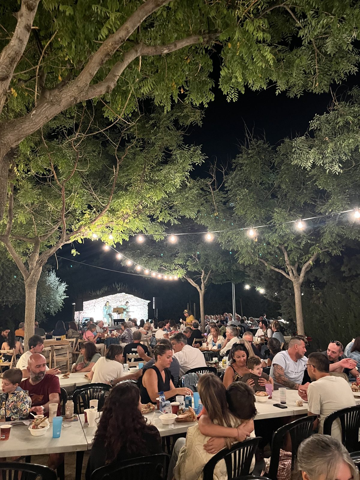 El sopar popular sota les llums, entre els arbres